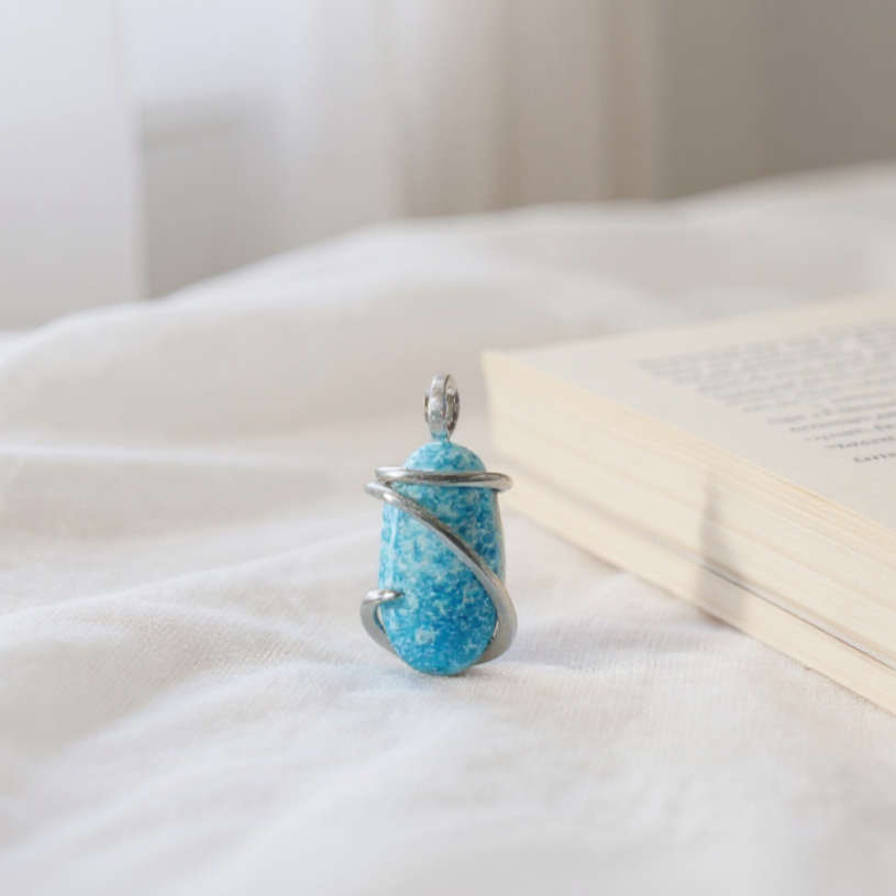 Turquoise stone pendant on a white surface with an open book in the background